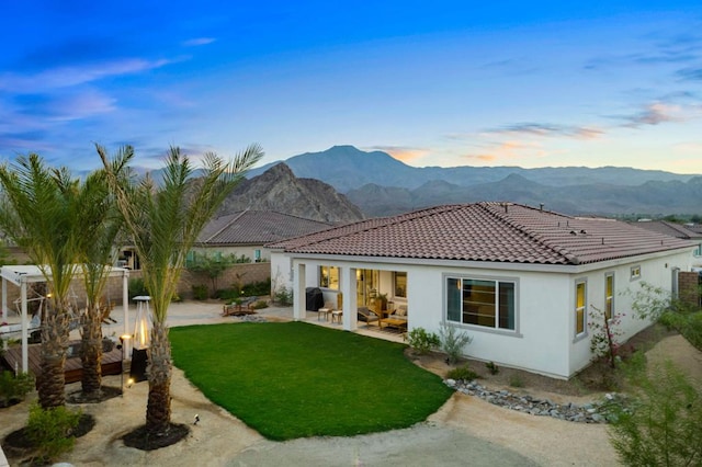 back house at dusk with a mountain view, a lawn, and a patio area