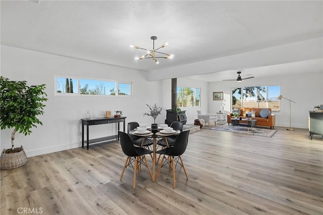 dining area featuring ceiling fan with notable chandelier, a wood stove, and light wood-type flooring