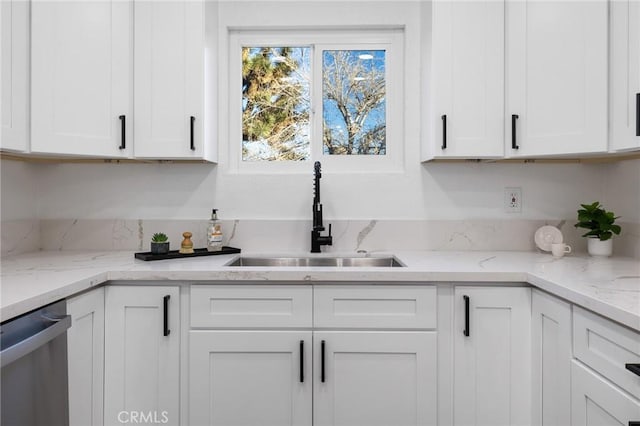 kitchen featuring stainless steel dishwasher, sink, white cabinets, and light stone countertops