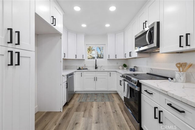 kitchen with light stone countertops, white cabinetry, stainless steel appliances, light hardwood / wood-style floors, and sink