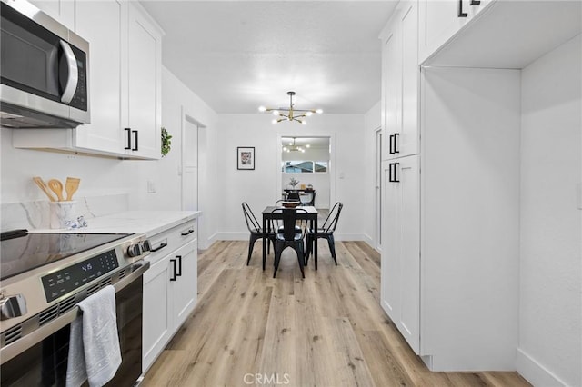 kitchen with light stone countertops, white cabinets, appliances with stainless steel finishes, and light hardwood / wood-style flooring