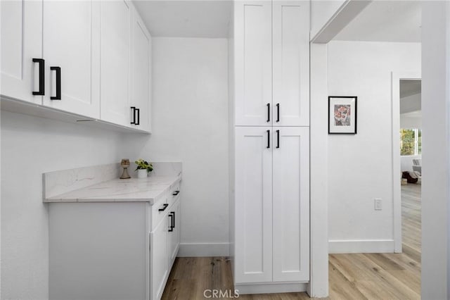 bar with white cabinets, light stone countertops, and light hardwood / wood-style floors