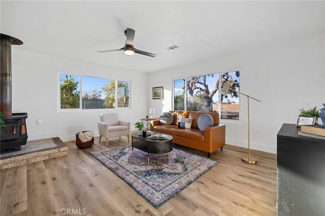 living room featuring ceiling fan, light hardwood / wood-style floors, and a wood stove