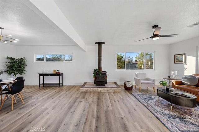 living room with ceiling fan, a wood stove, and light hardwood / wood-style flooring