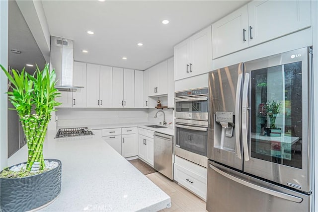 kitchen with white cabinets, appliances with stainless steel finishes, sink, ventilation hood, and light wood-type flooring