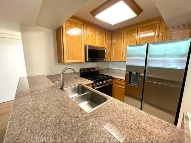 kitchen with light stone countertops, appliances with stainless steel finishes, kitchen peninsula, and sink