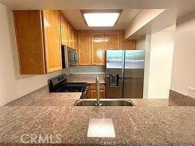 kitchen with light stone countertops, sink, appliances with stainless steel finishes, and kitchen peninsula