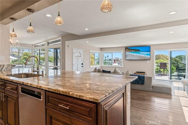 kitchen featuring sink, dishwasher, hanging light fixtures, a wealth of natural light, and light stone countertops