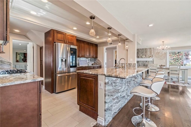 kitchen with a kitchen island with sink, light stone countertops, decorative light fixtures, and stainless steel appliances