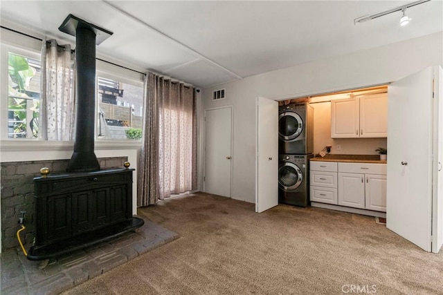 interior space featuring white cabinetry, stacked washer / drying machine, carpet floors, and a wood stove