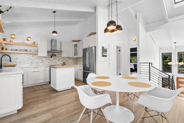 kitchen featuring pendant lighting, wall chimney range hood, white cabinetry, and stainless steel fridge