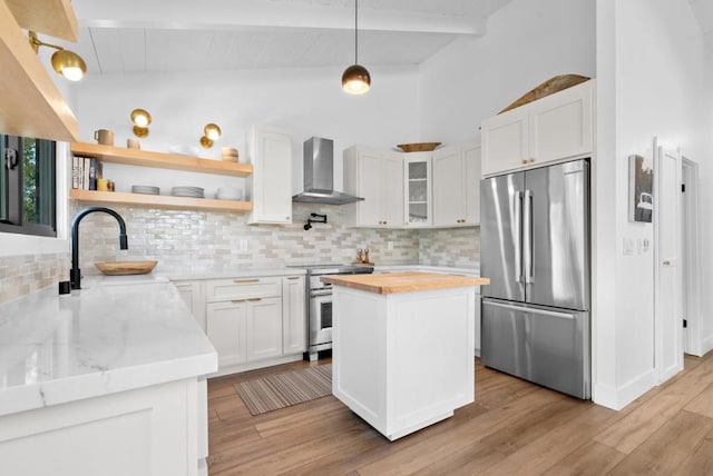 kitchen with stainless steel appliances, lofted ceiling with beams, white cabinets, a kitchen island, and wall chimney exhaust hood