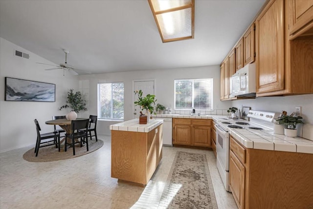 kitchen with lofted ceiling, white appliances, tile countertops, a kitchen island, and ceiling fan