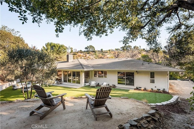 rear view of property featuring a chimney, a lawn, a patio area, and stucco siding