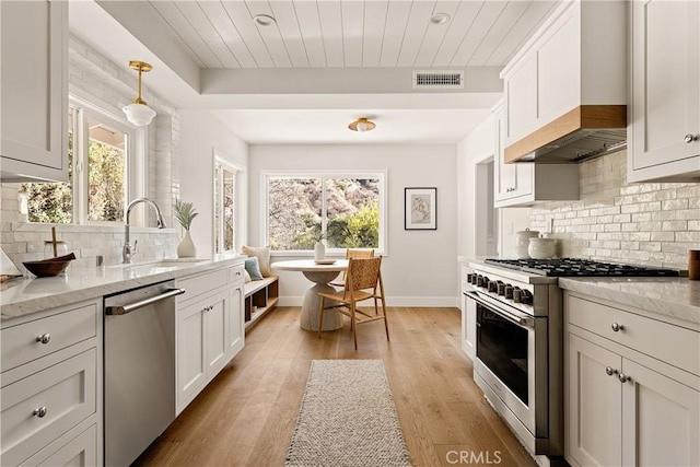 kitchen featuring light stone counters, stainless steel appliances, custom range hood, and white cabinets