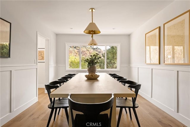 dining space featuring wainscoting, a decorative wall, and light wood finished floors