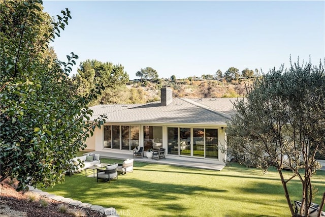 rear view of house with roof with shingles, a patio, a chimney, a lawn, and an outdoor hangout area