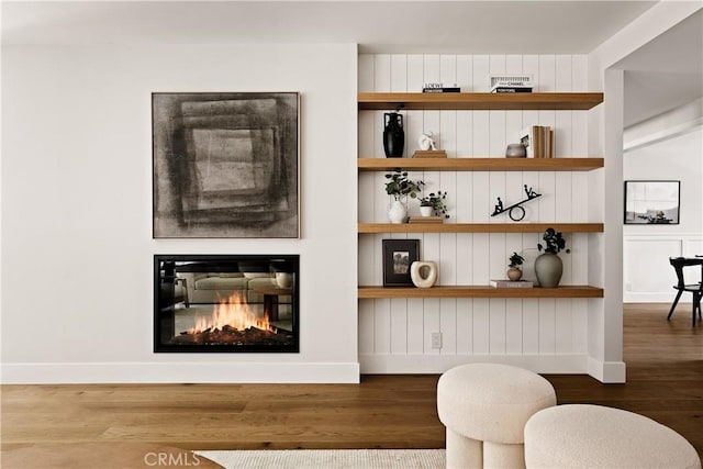 interior space featuring baseboards, a glass covered fireplace, and wood finished floors