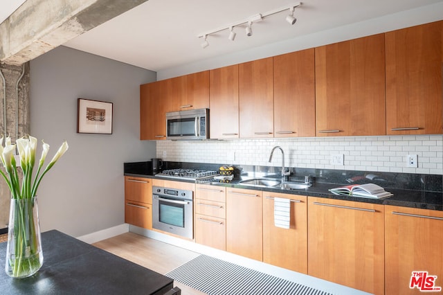 kitchen featuring dark stone countertops, light hardwood / wood-style floors, decorative backsplash, sink, and appliances with stainless steel finishes