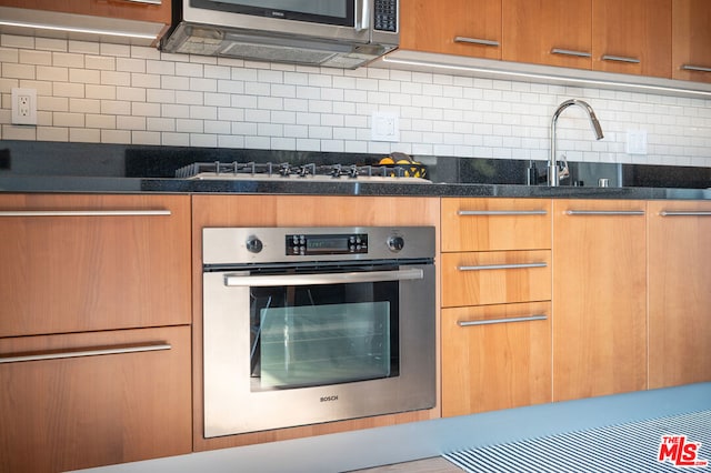 kitchen with stainless steel appliances, dark stone counters, tasteful backsplash, sink, and range hood