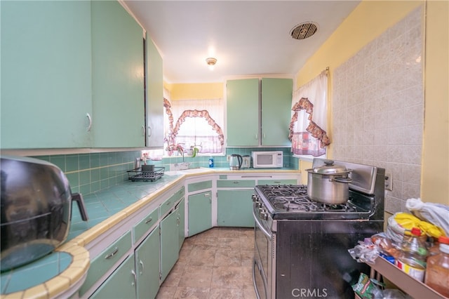 kitchen featuring tile countertops, tasteful backsplash, stainless steel range with gas cooktop, and sink