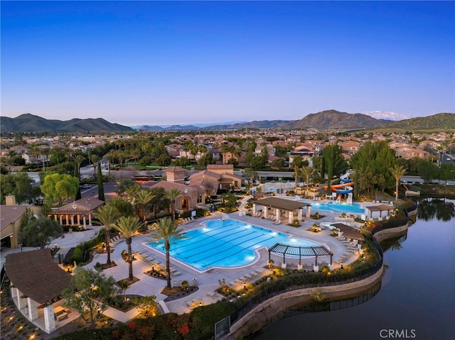 pool at dusk with a water slide, a water and mountain view, and a patio