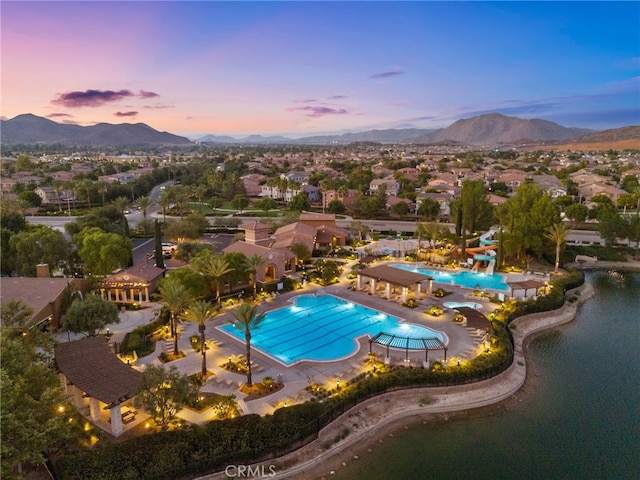 pool at dusk featuring a water and mountain view and a patio