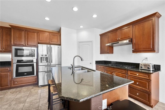 kitchen featuring stainless steel appliances, dark stone countertops, an island with sink, and sink