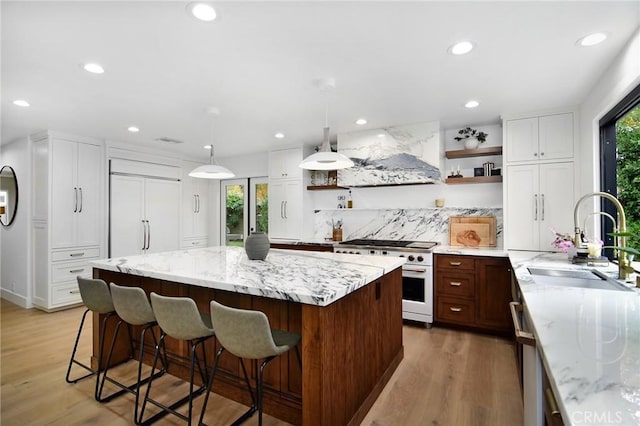 kitchen with white cabinetry, wall chimney range hood, sink, hanging light fixtures, and high quality appliances