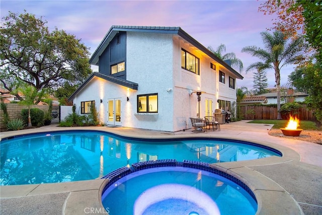 pool at dusk featuring grilling area, an outdoor fire pit, a patio, and an in ground hot tub