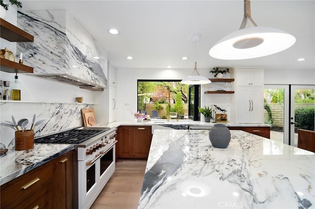 kitchen with decorative light fixtures, custom exhaust hood, decorative backsplash, light stone countertops, and range with two ovens