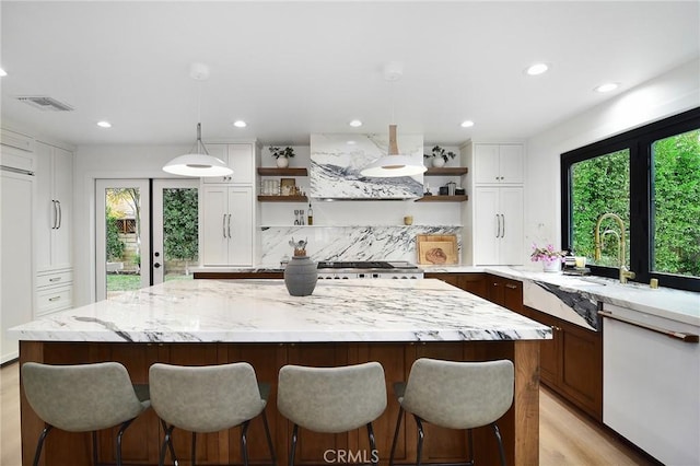 kitchen with backsplash, wall chimney range hood, hanging light fixtures, light stone countertops, and white cabinets