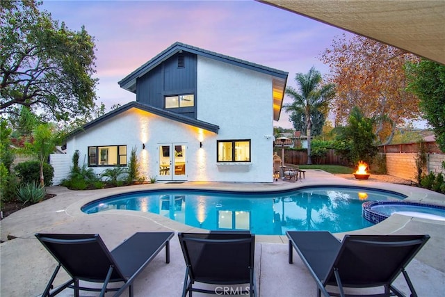 pool at dusk featuring an outdoor fire pit, an in ground hot tub, and a patio