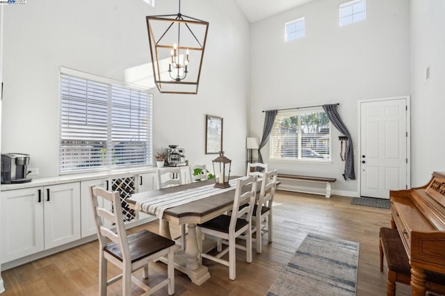 dining room with a towering ceiling, a notable chandelier, and light wood-type flooring