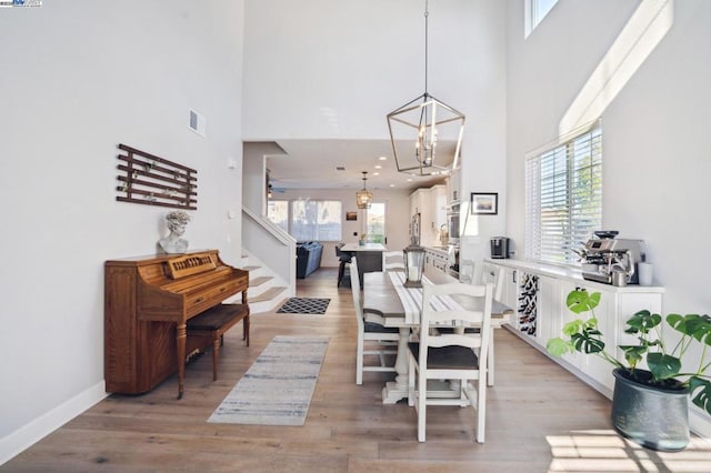 dining room featuring ceiling fan with notable chandelier, a high ceiling, and light hardwood / wood-style floors