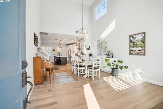 dining area with an inviting chandelier, light hardwood / wood-style flooring, and a high ceiling