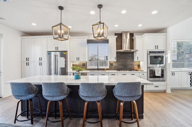 kitchen featuring a spacious island, white cabinets, stainless steel appliances, and wall chimney exhaust hood