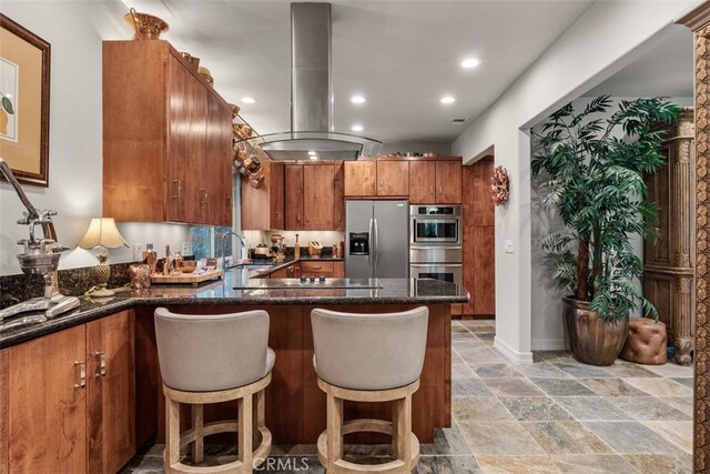 kitchen featuring kitchen peninsula, island exhaust hood, appliances with stainless steel finishes, a kitchen breakfast bar, and sink