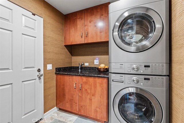 laundry room featuring cabinets, sink, and stacked washer and clothes dryer