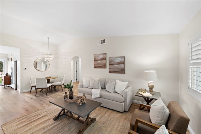 living room with an inviting chandelier, lofted ceiling, and light hardwood / wood-style flooring