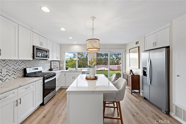 kitchen with white cabinets, appliances with stainless steel finishes, a center island, tasteful backsplash, and hanging light fixtures