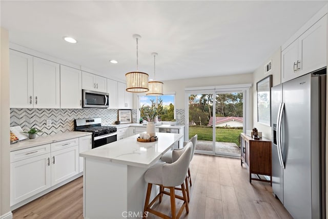 kitchen with decorative light fixtures, a kitchen island, light stone countertops, appliances with stainless steel finishes, and white cabinets