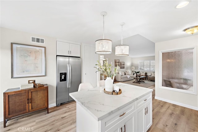 kitchen featuring light stone countertops, pendant lighting, white cabinets, a center island, and stainless steel fridge