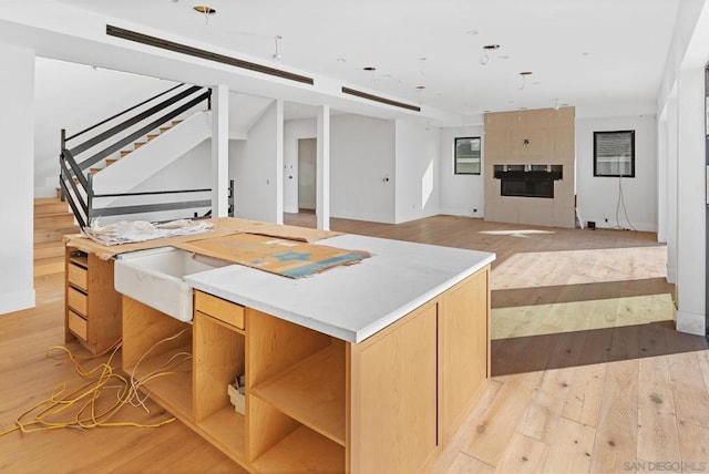 kitchen with a kitchen island, light brown cabinetry, a fireplace, and light hardwood / wood-style flooring