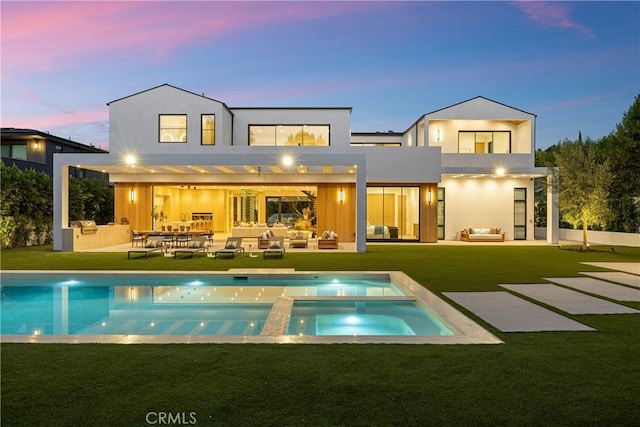 back house at dusk with a pool with hot tub, an outdoor kitchen, outdoor lounge area, and a patio