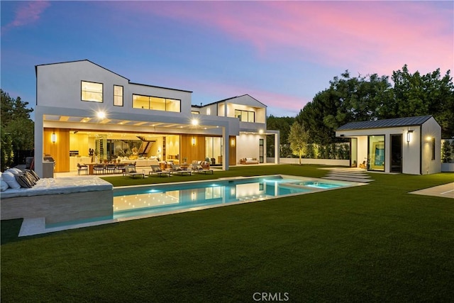 back house at dusk featuring a lawn, an outdoor living space, an outdoor structure, and a patio