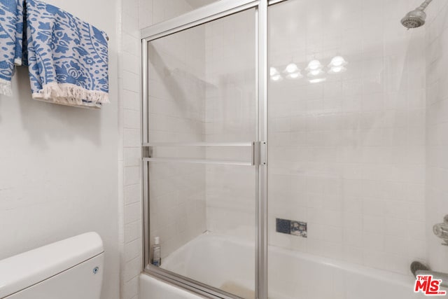 bathroom featuring combined bath / shower with glass door and toilet