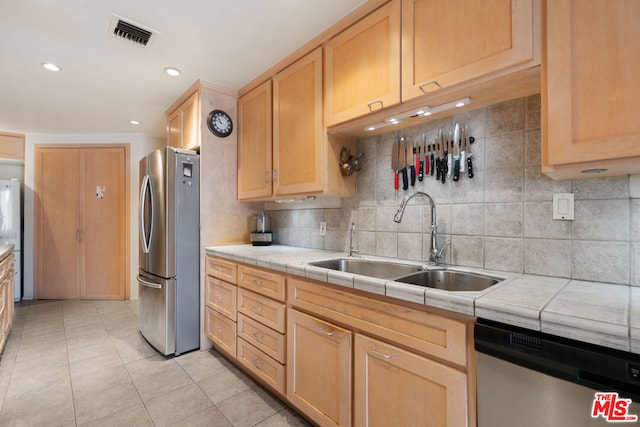 kitchen featuring tile countertops, appliances with stainless steel finishes, decorative backsplash, light brown cabinetry, and sink