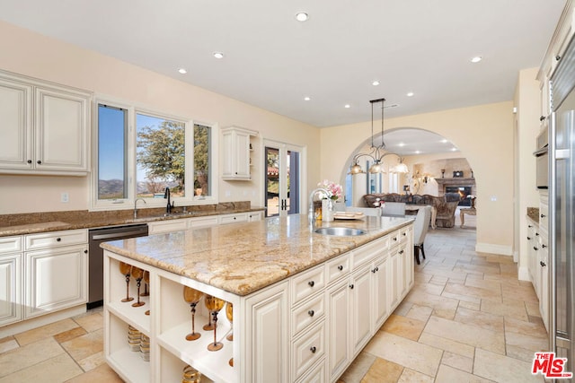 kitchen with light stone countertops, an island with sink, sink, hanging light fixtures, and stainless steel dishwasher