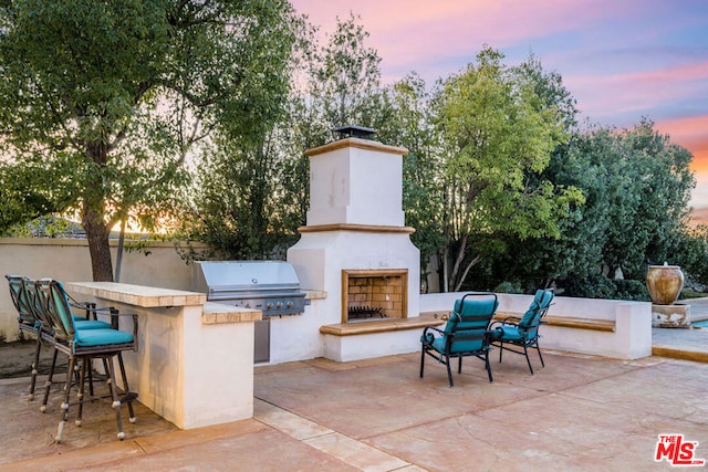 patio terrace at dusk with an outdoor bar, area for grilling, exterior kitchen, and exterior fireplace